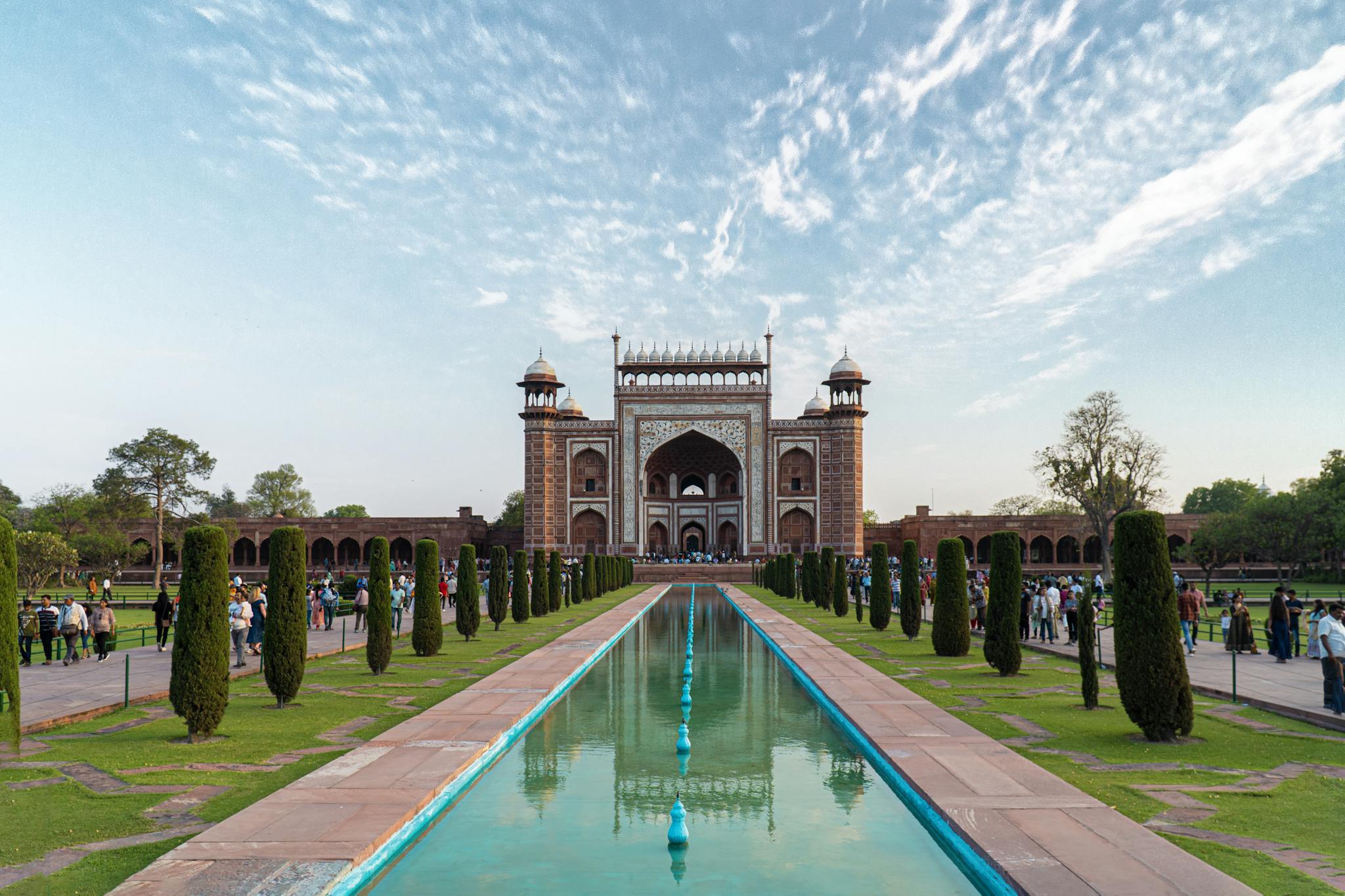 Breathtaking view of the main entrance gate to the Taj Mahal during sunset, featuring lush gardens.